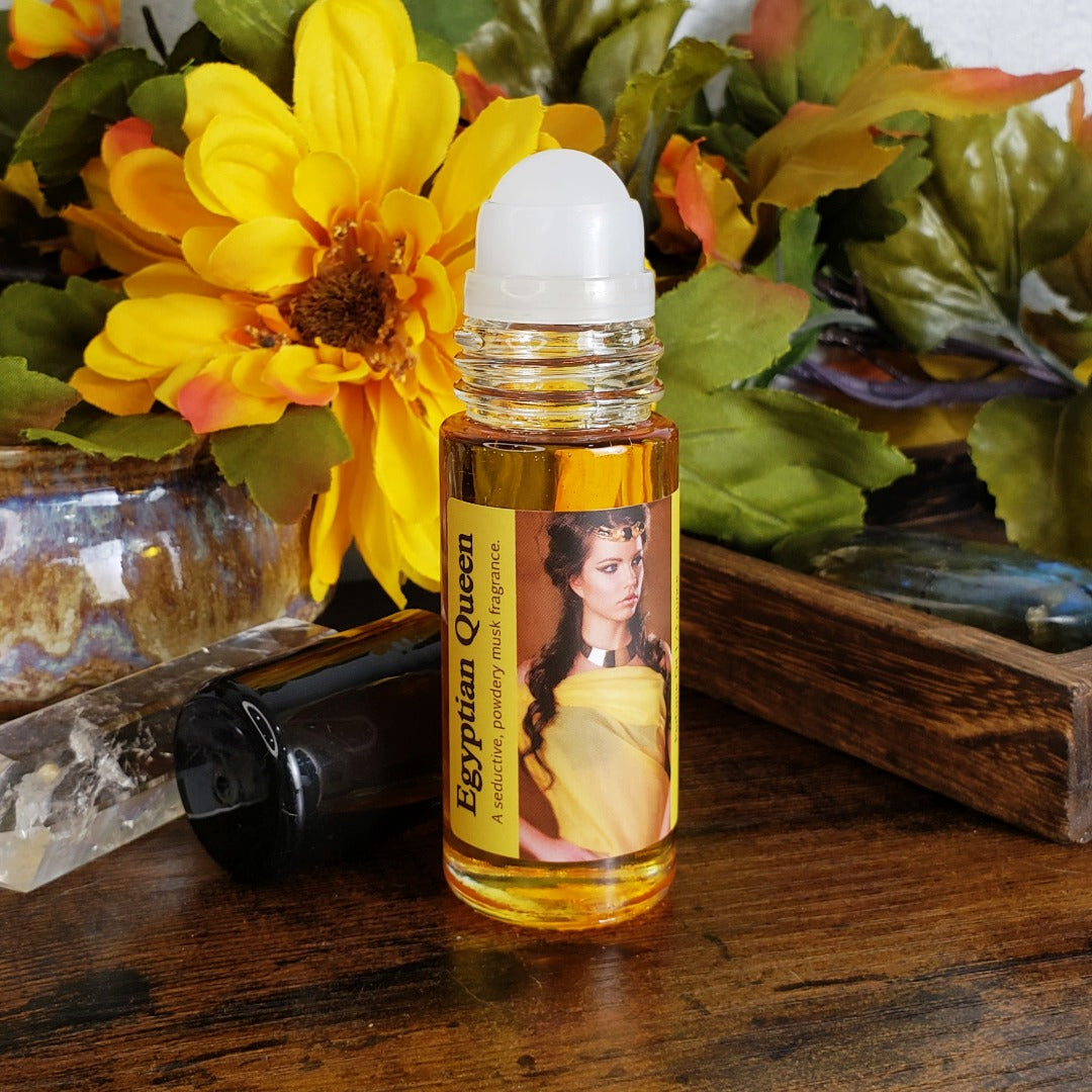 large one ounce bottle of egyptian queen perfume oil with the roller ball showing, a seductive musk fragrance oil, on a table with flowers in the background