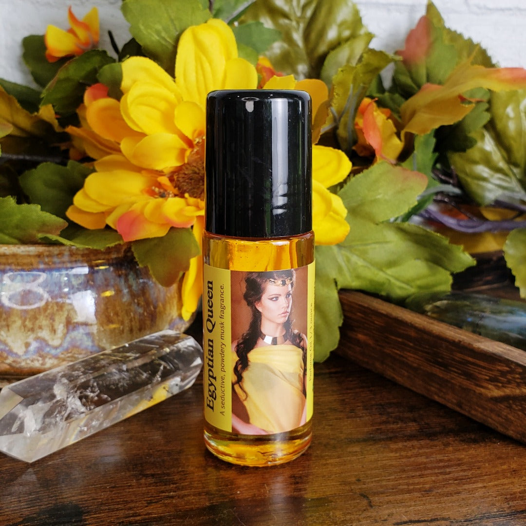 large one ounce bottle of egyptian queen perfume oil, a seductive musk fragrance oil, on a table with flowers in the background