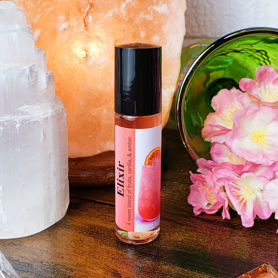 Roll-on bottle labeled 'Elixir' with pink label on a wooden surface with crystals and flowers.
