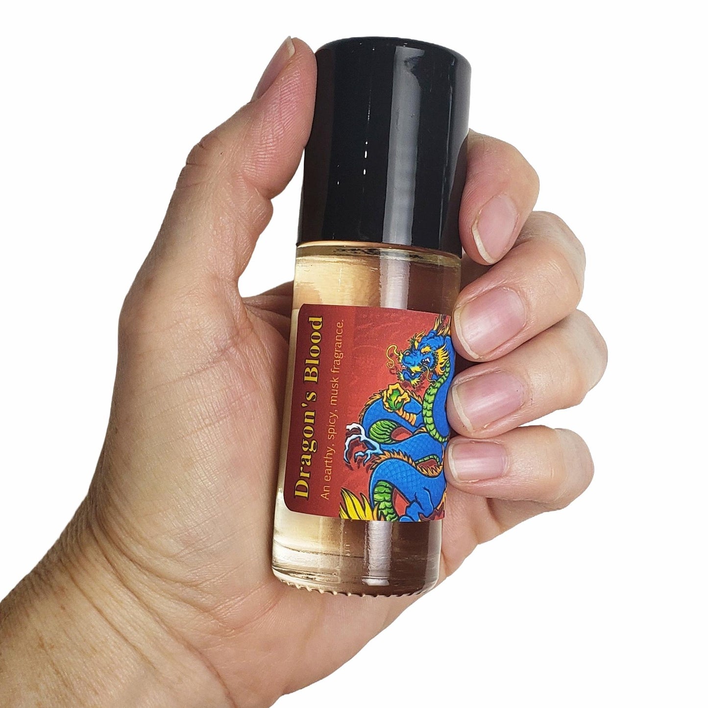 A hand holding a small glass bottle of Dragon's Blood fragrance oil with a black cap and a red label featuring a blue dragon illustration, against a plain white background.