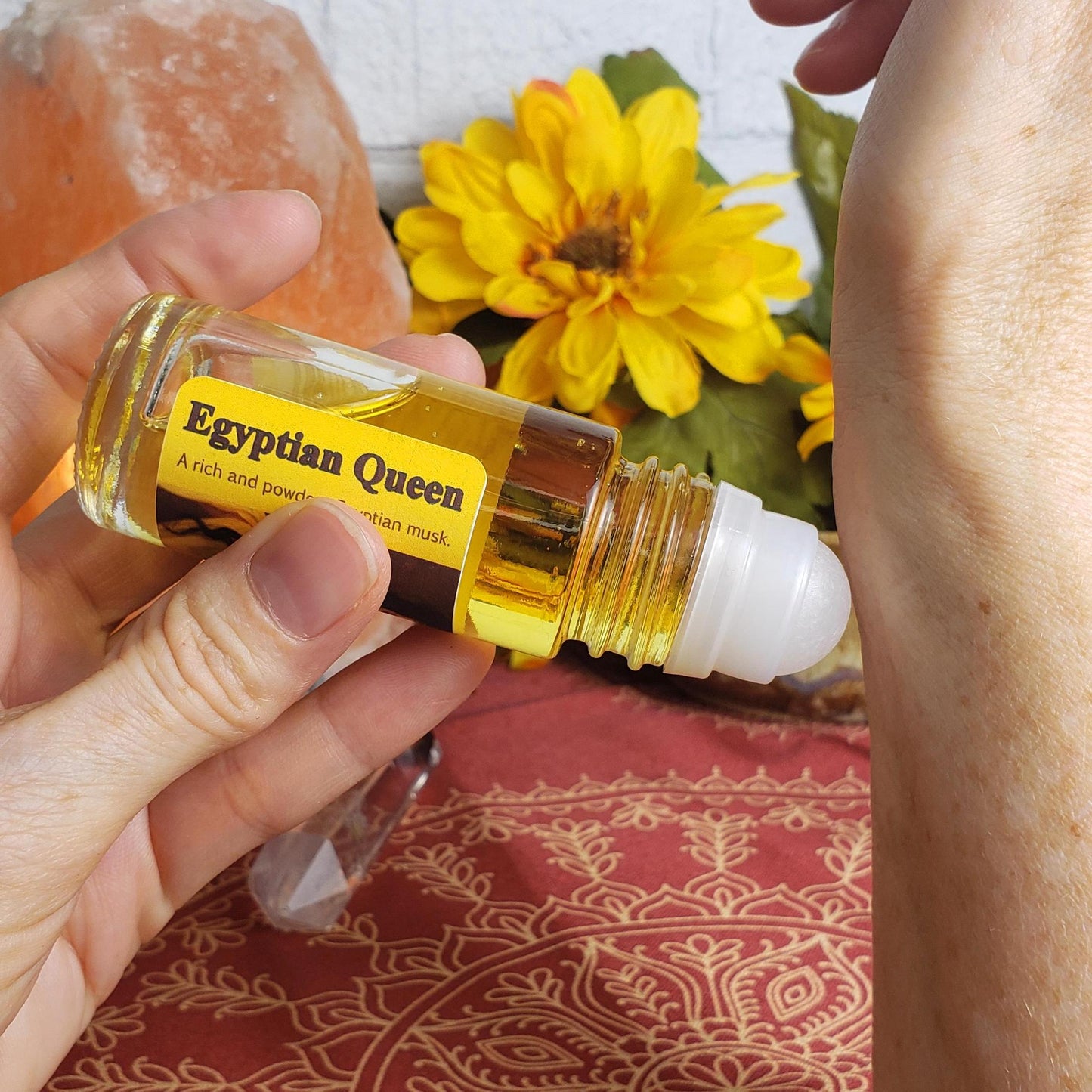 applying a roll-on of egyptian queen perfume oil to the wrist, with the larger one ounce bottle