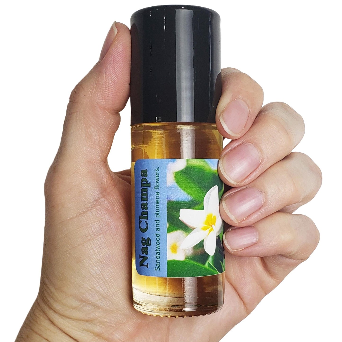 A hand holding a small glass roller bottle of Nag Champa perfume oil with a black cap and a blue-and-white floral label, showing the size of the bottle in a hand. 
