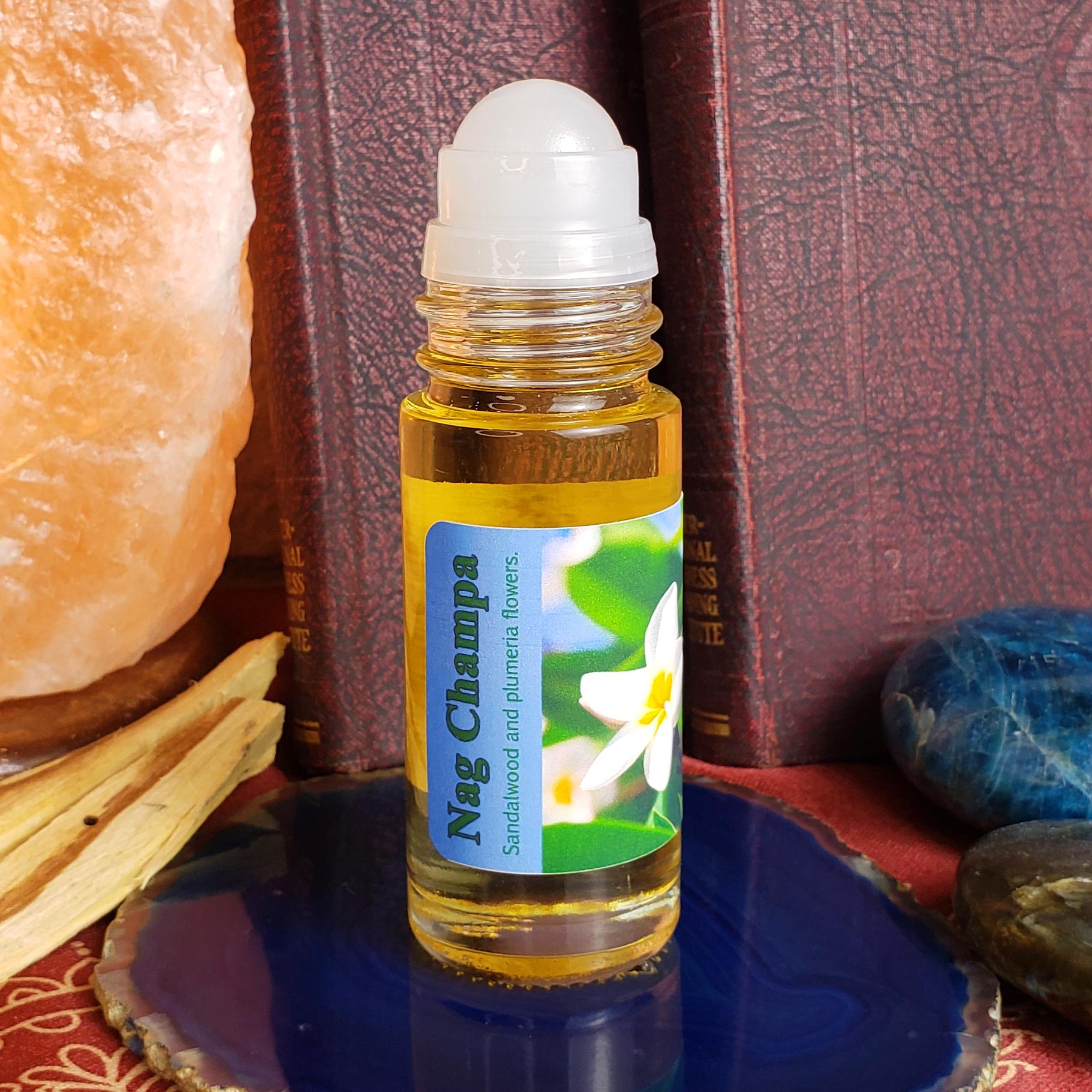 A 1 ounce glass bottle of Neg Champa essential oil or rollerball fragrance with a white cap, standing on a blue stone plate. The bottle has a label reading 'Neg Champa' with a flower photo.