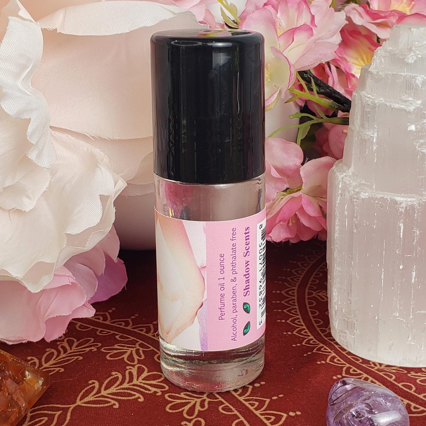 A large 1 ounce bottle of Love perfume oil with pink label and black cap covering the rollerball.