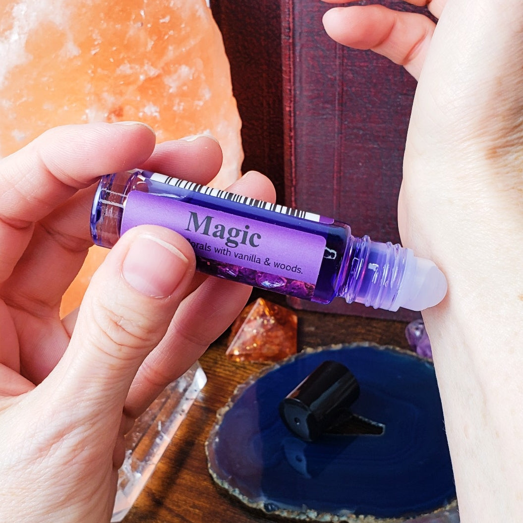 Purple rollerball bottle labeled 'Magic' held by a hand applying the perfume oil to the wrist
