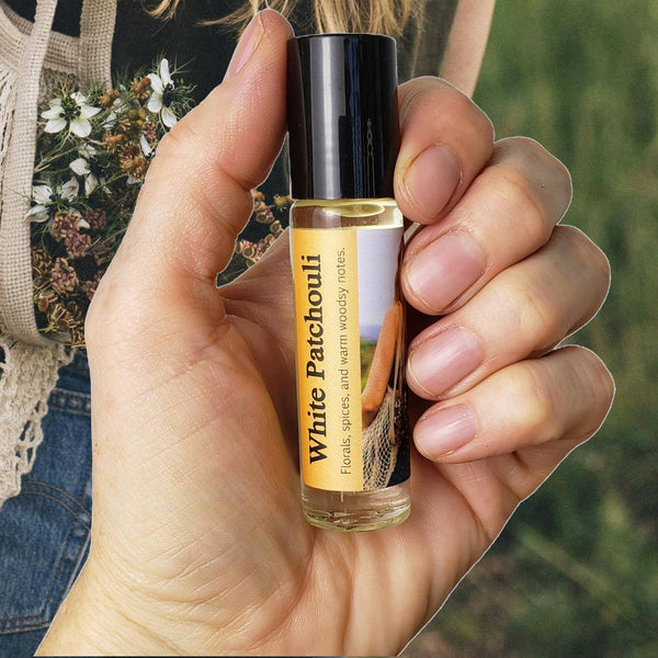 White Patchouli perfume oil bottle held in a hand against a floral background